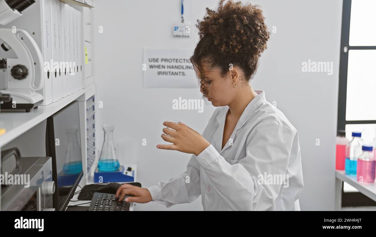 Hispanische Frau mit lockigem Haar, die in einem Labor arbeitet und eine chemische Probe im Haus untersucht. Stockfoto