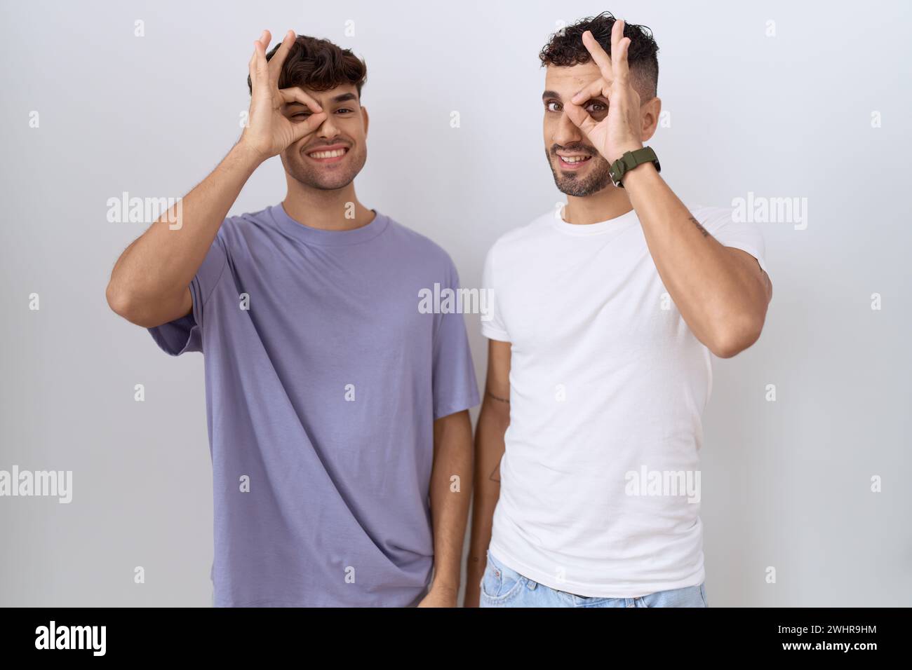 Homosexuelles schwules Paar, das über weißem Hintergrund steht und eine gute Geste macht, mit lächelnder Hand, mit Blick durch die Finger mit glücklichem Gesicht. Stockfoto