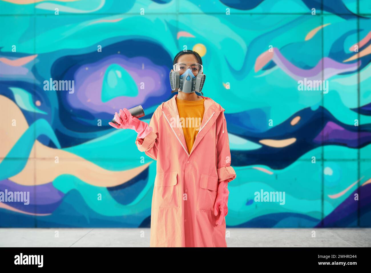 Graffiti-Künstlerin in Atemschutzmaske, die neben der Wand steht, mit ihren Gemälden, die in die Kamera schauen Stockfoto