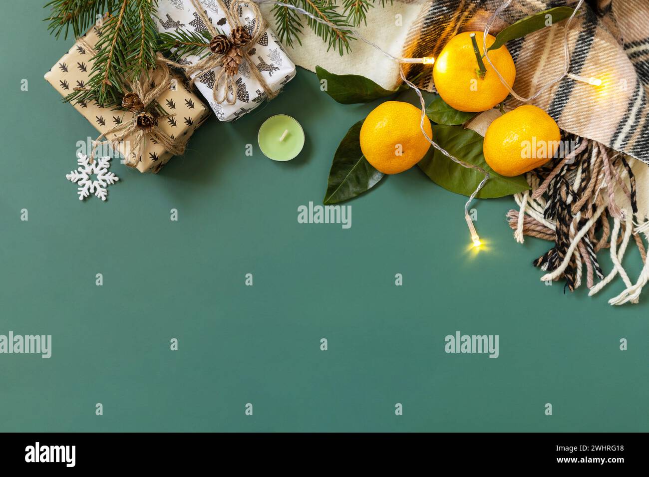 Winterkomposition mit Tannenzweigen, Geschenk, Schal und Mandarinen auf grünem Hintergrund. Gemütliche Winterstimmung. Blick von oben. Co Stockfoto