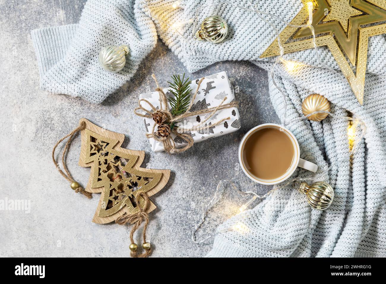 Neujahrs- oder Weihnachtskomposition. Tasse Kaffee, weihnachtsstern, Strickdecke, Girlande und Geschenk auf grauem Hintergrund. Wint Stockfoto