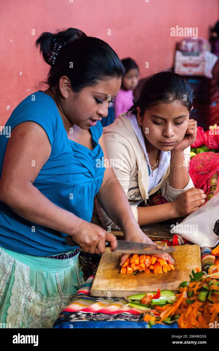 Chichicastenango, Guatemala.  Quiche (Kiche, k ' iche ') Mädchen schneiden Karotten, Salat, Markthalle machen. Stockfoto