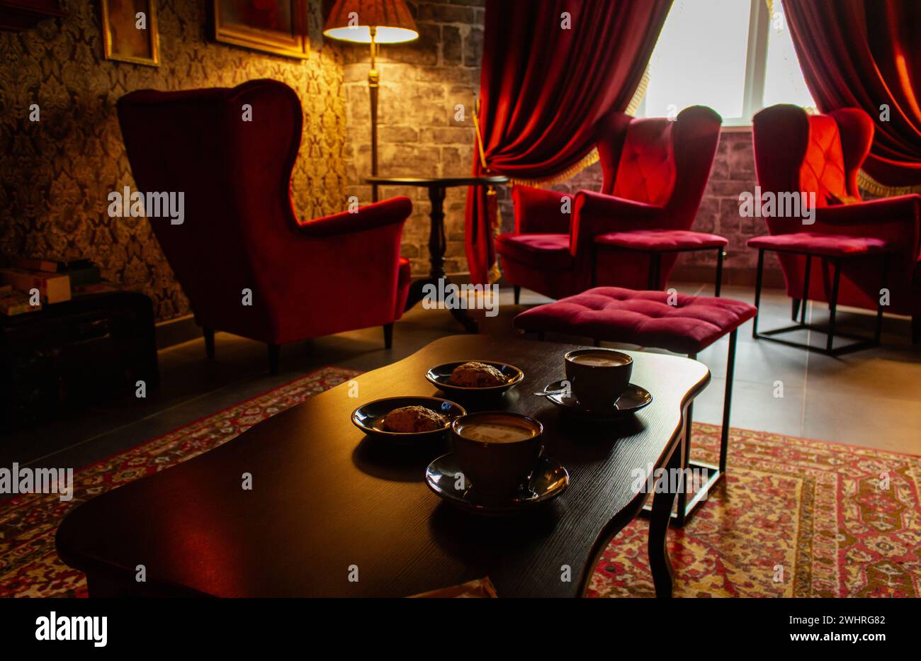 Rote Sessel mit Kaffeetassen auf dem Tisch in gemütlicher klassischer Einrichtung. Antikes Wohnzimmer mit roten Vorhängen und Sesseln. Schloss Hogwarts. Stockfoto