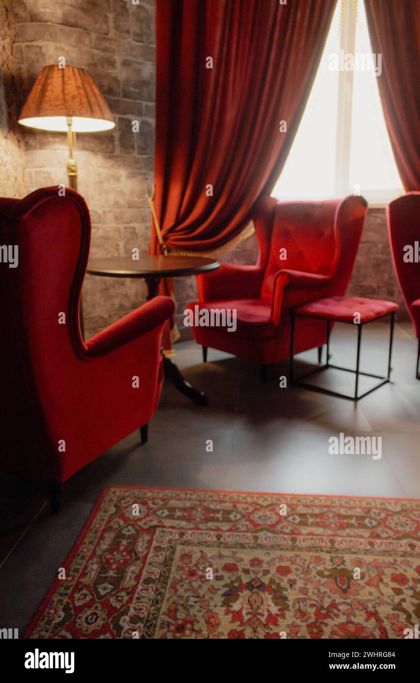 Rote Sessel und Tisch mit Lampe in gemütlicher klassischer Einrichtung. Antikes Wohnzimmer mit roten Vorhängen und Sesseln. Schloss Hogwarts. Stockfoto
