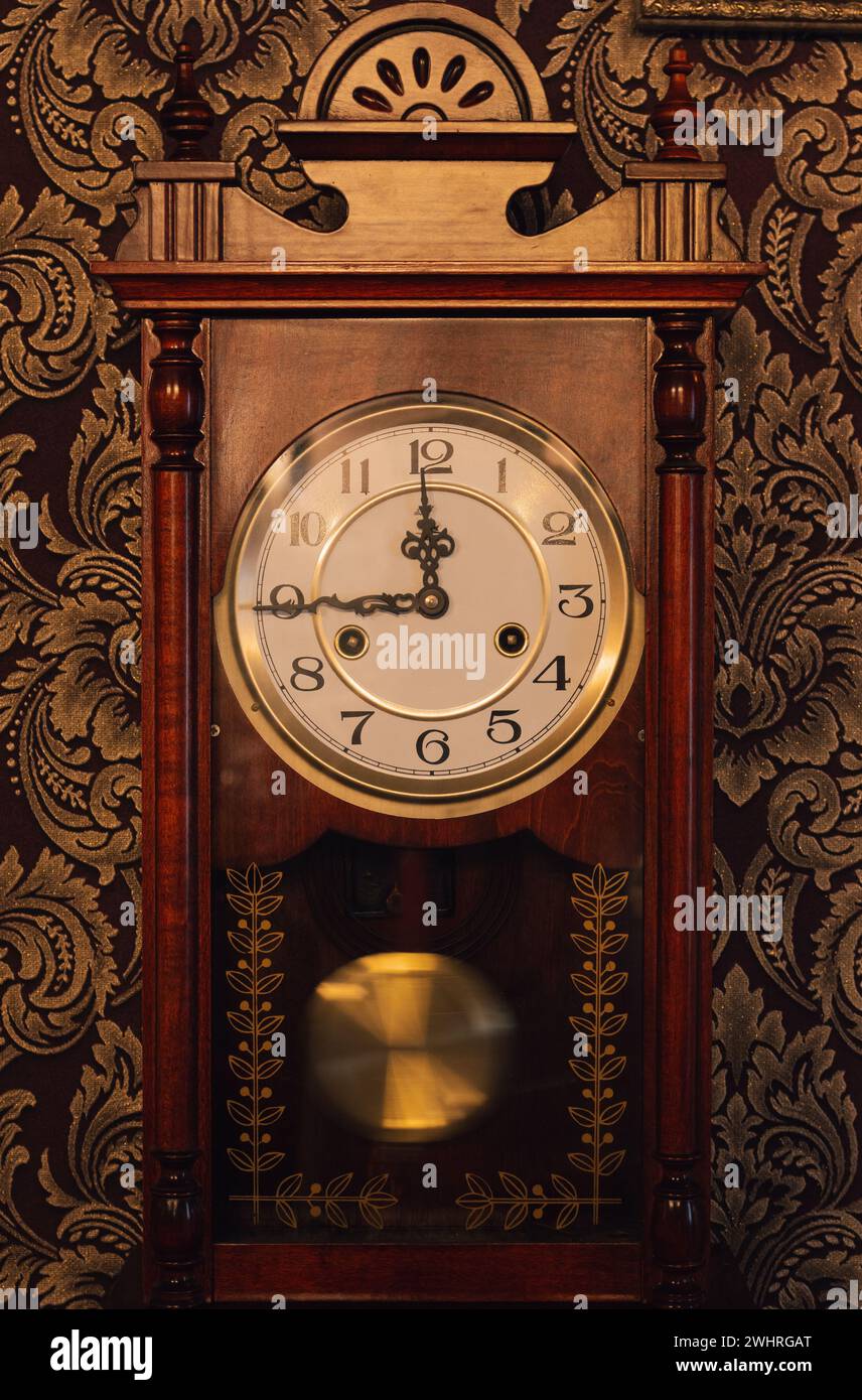 Vintage-Uhr mit Pendel an der Wand. Nostalgiekonzept. Antike Uhr mit Ticker. Altmodisches Zifferblatt mit Pfeilen. Klassisches Zimmerdesign. Stockfoto