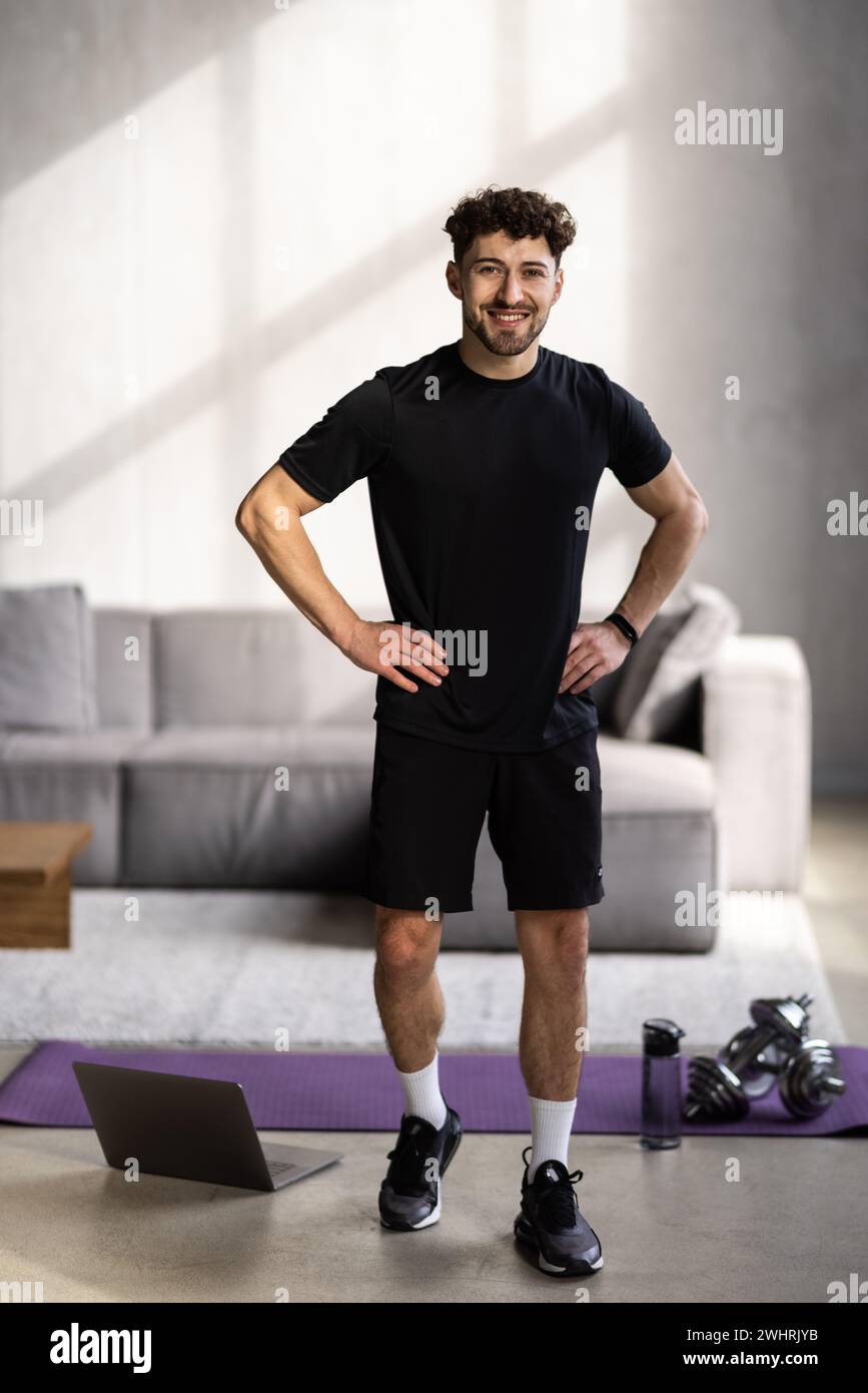 Athlet man trainiert hart in leerem Fitnessstudio oder zu Hause vor dem Laptop. Selbstisolierte und motivierte Aufwärmübungen für junge Männer Stockfoto