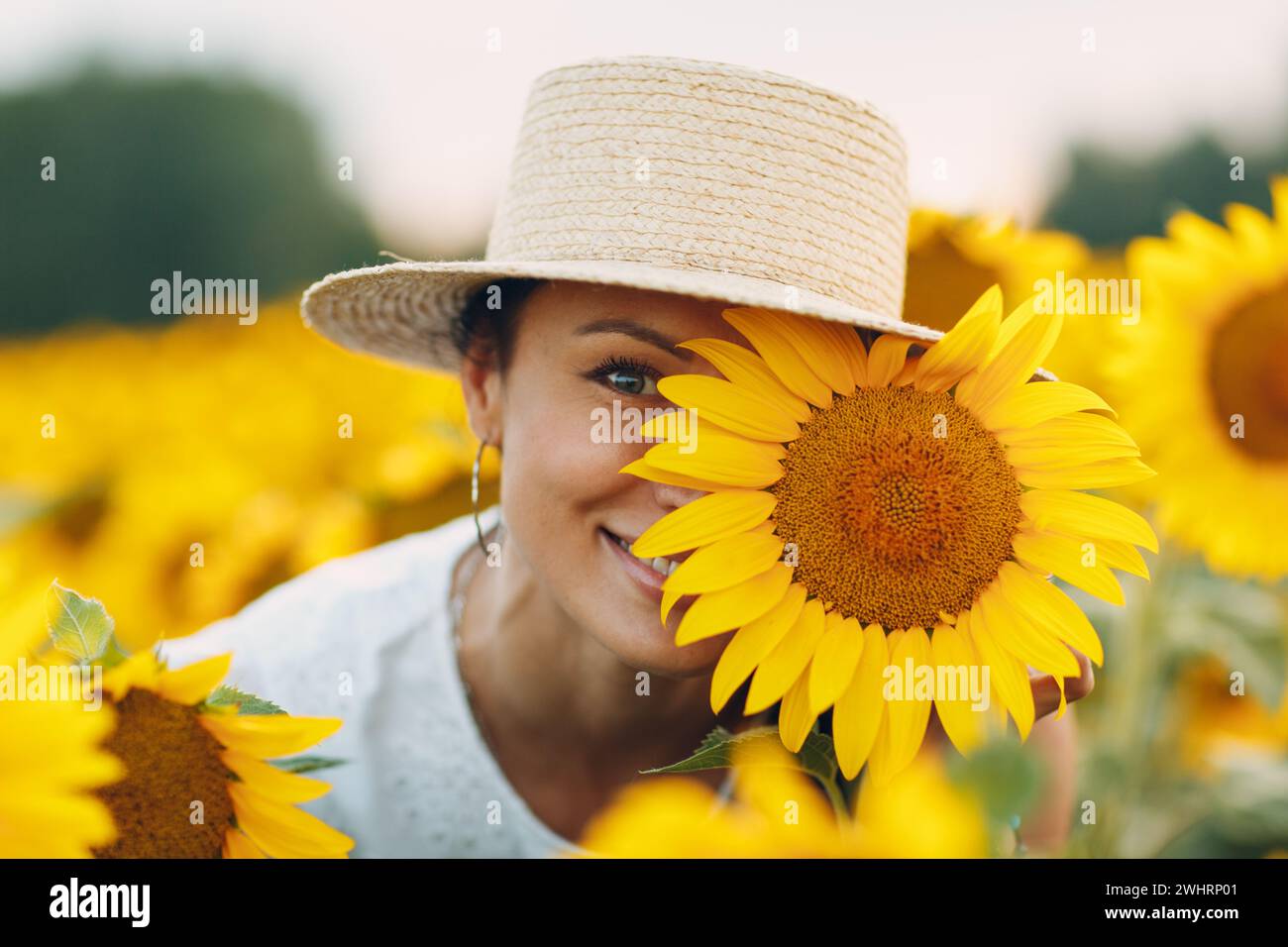 Schöne lächelnde junge Frau in einem Hut mit Blume auf Ihr Auge und Gesicht auf einem Feld von Sonnenblumen Stockfoto