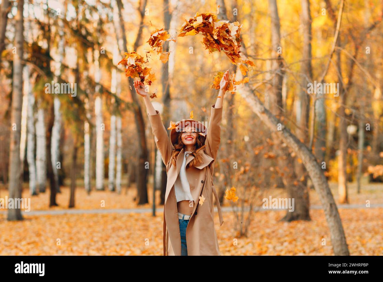 Mädchen im wunderschönen Herbstpark wirft Orangenblätter auf. Herbst-Mode. Stockfoto