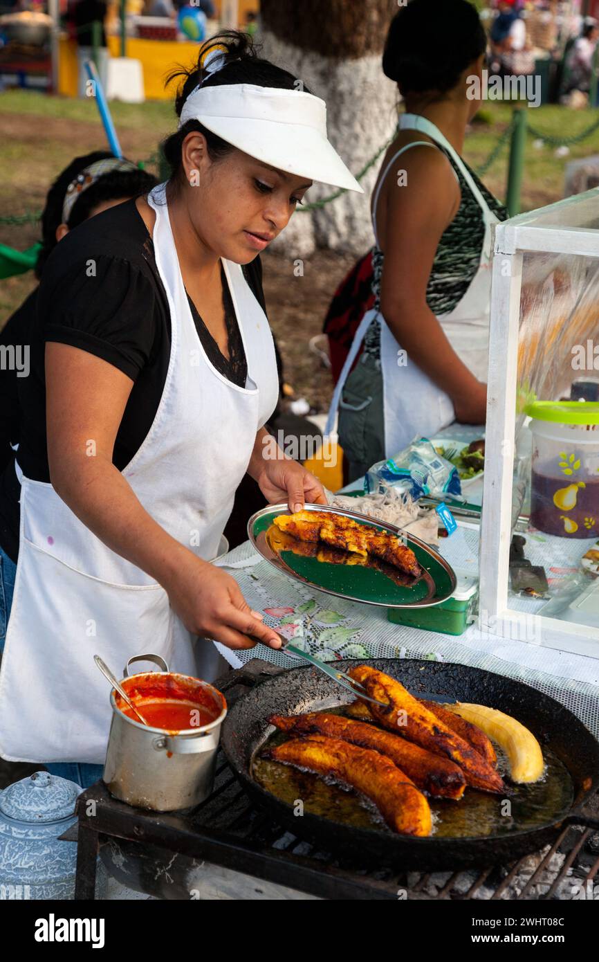 Antigua, Guatemala. Junge Frau serviert gebratene Bananen an einem Food Stand. Stockfoto