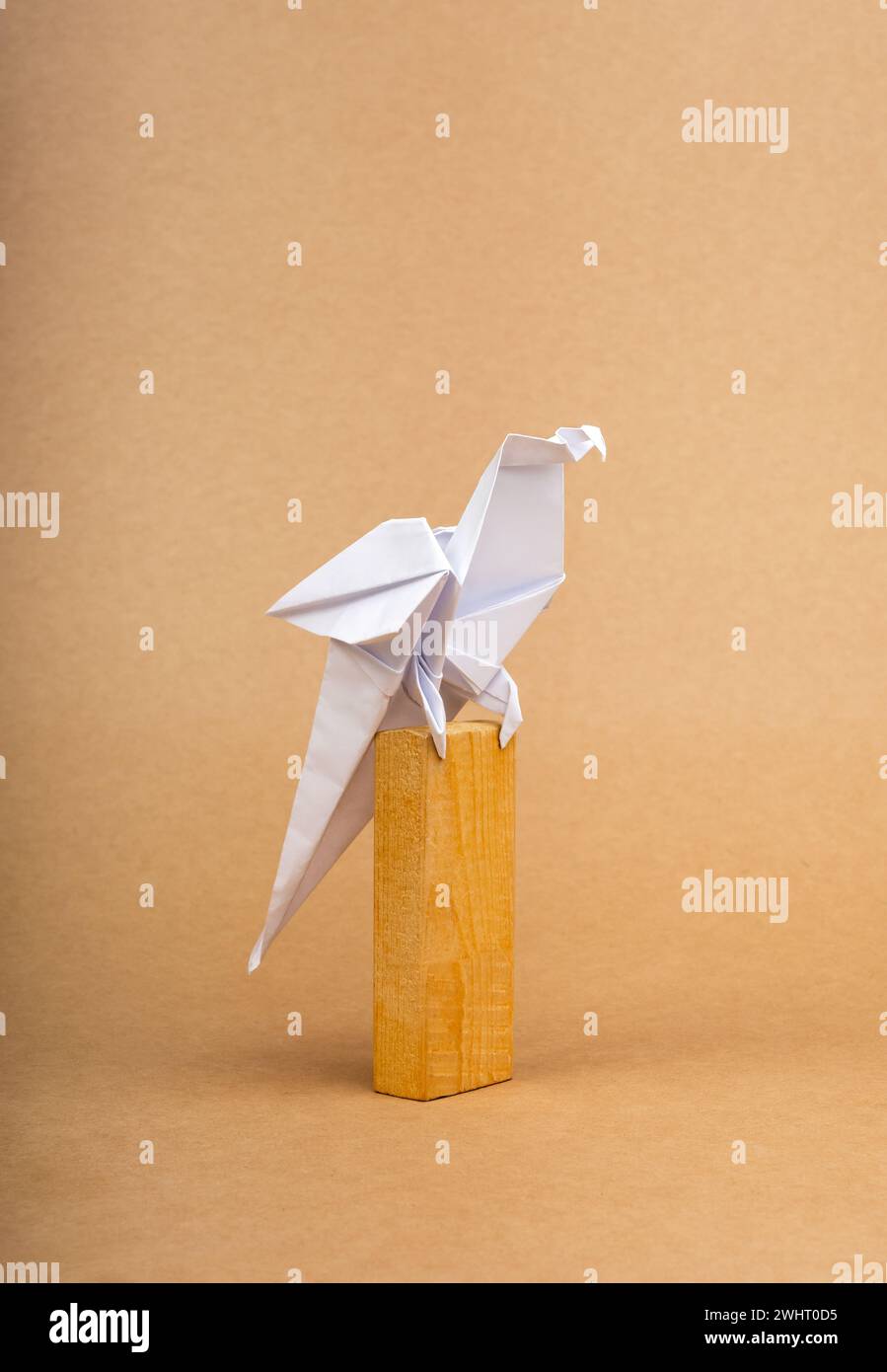 Ein weißes Papageienvogelpapier, das auf Holzstock-Block steht, isoliert auf ökologischem braunem Kraftpapier-Hintergrund. Origami-Kunst im Handwerkskunst-Stil auf Recyclingpapier. A Stockfoto
