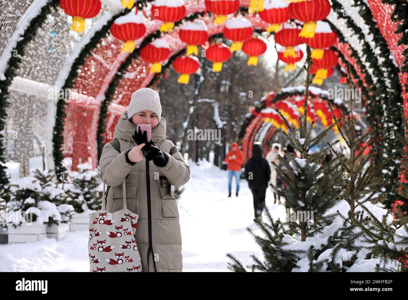 Mädchen mit Smartphone, das auf dem Hintergrund der chinesischen Neujahrsdekorationen in der Winterstadt läuft Stockfoto