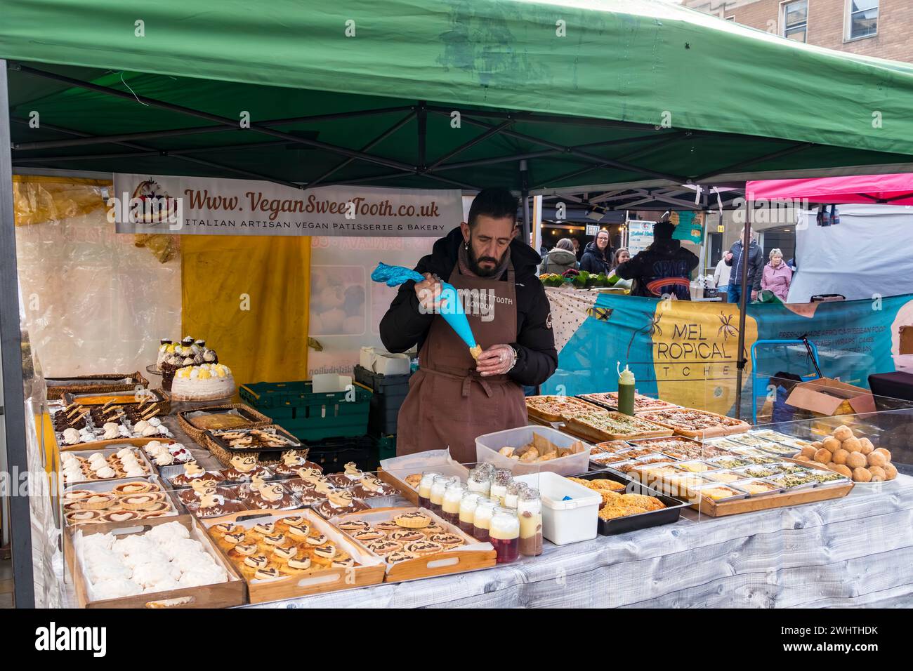 Stallhalter, der vegane Rahmbrötchen auf veganer Konditorei und Bäckereistand füllt, Cornhill Market, Lincoln City, Lincolnshire, England, UK Stockfoto
