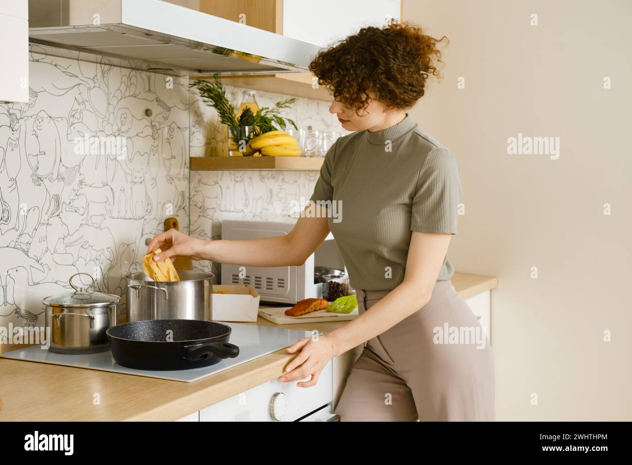 Hausfrau fügt Pappardelle Pasta in den Topf mit kochendem Wasser in der hellen Küche Stockfoto