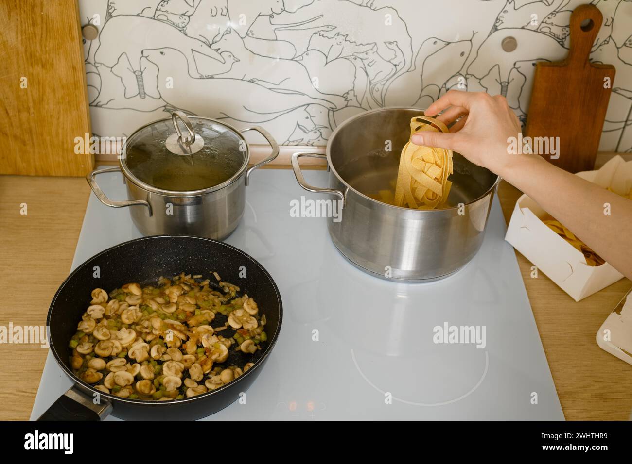 Blick von oben auf die weibliche Hand, die Pappardelle-Pasta in den Topf mit kochendem Wasser geben Stockfoto