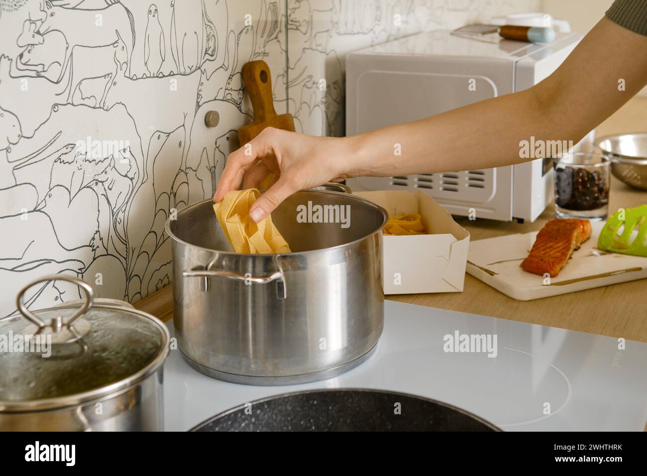 Weibliche Hand fügt Pappardelle-Pasta in einen Topf mit kochendem Wasser Stockfoto