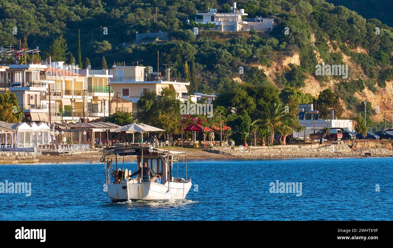 Fischerboot an einer idyllischen Mittelmeerküste mit Stadt und Hügeln im Hintergrund, Gythio, Mani, Peloponnes, Griechenland Stockfoto