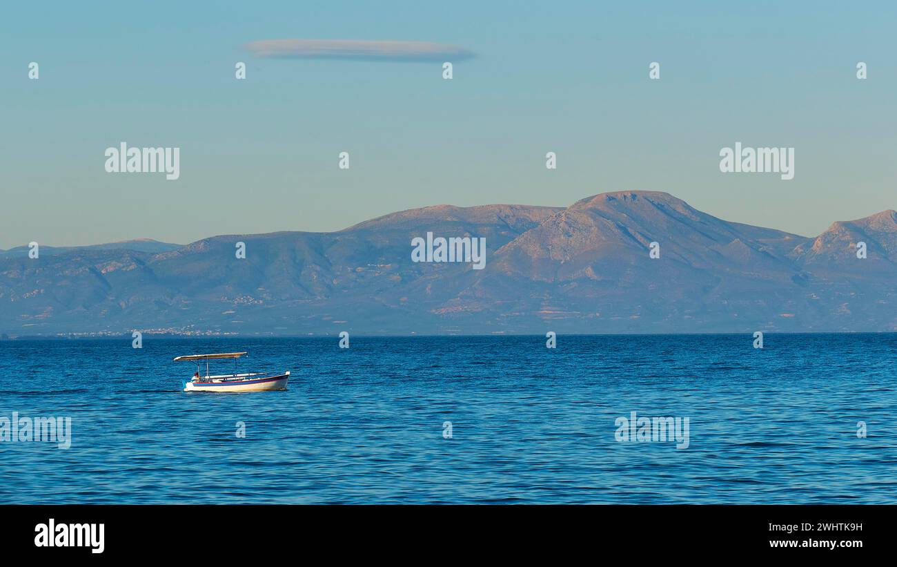 Einsames Boot auf dem breiten blauen Meer mit Bergen im Hintergrund und klarem Himmel, Gythio, Mani, Peloponnes, Griechenland Stockfoto