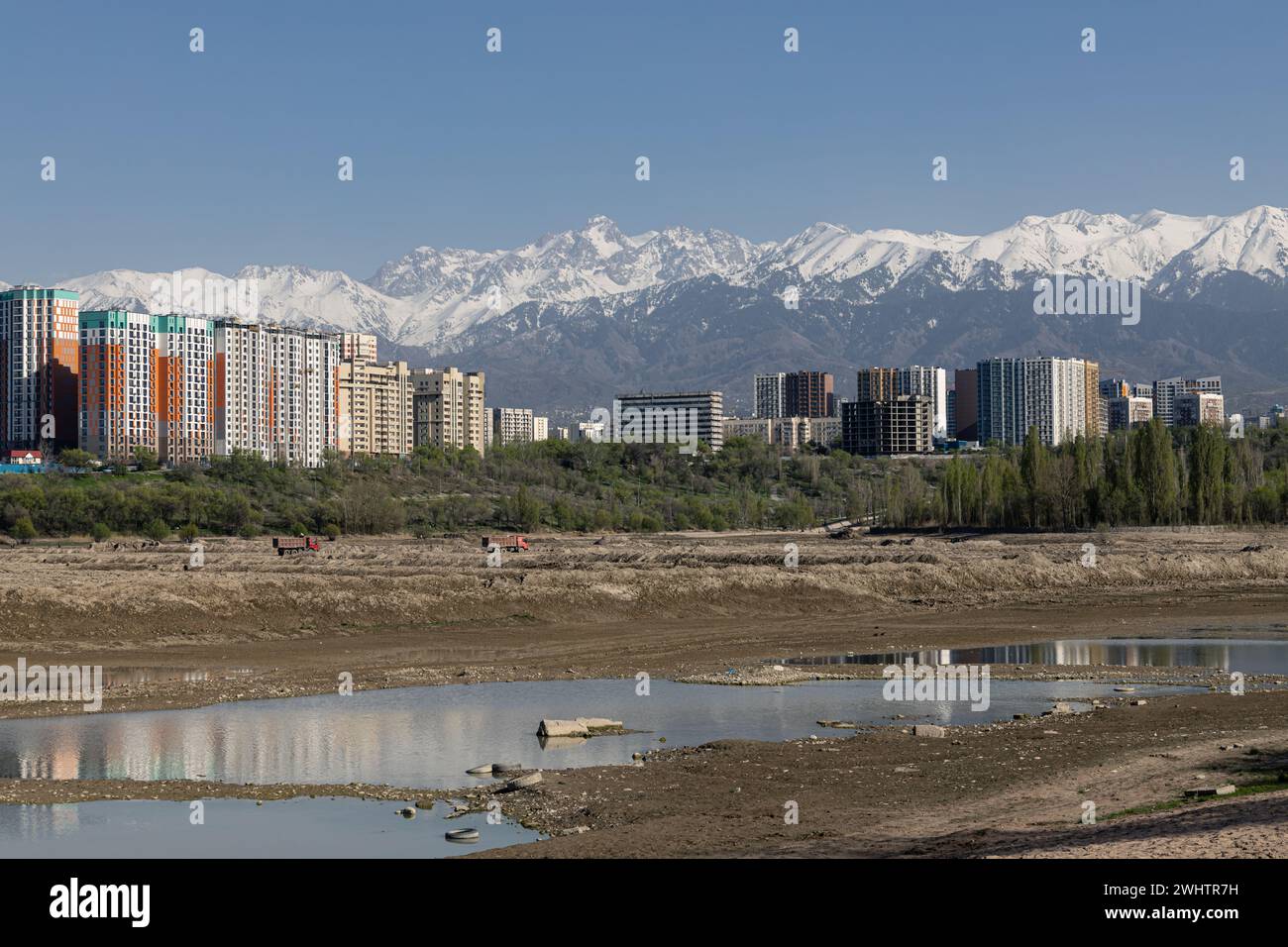 Speicherreservoir Sayran-See, Almaty, Kasachstan. Leerer City Sandstrand mit entwässertem Teich. Wohnhäuser und hohe schneebedeckte Montage Stockfoto