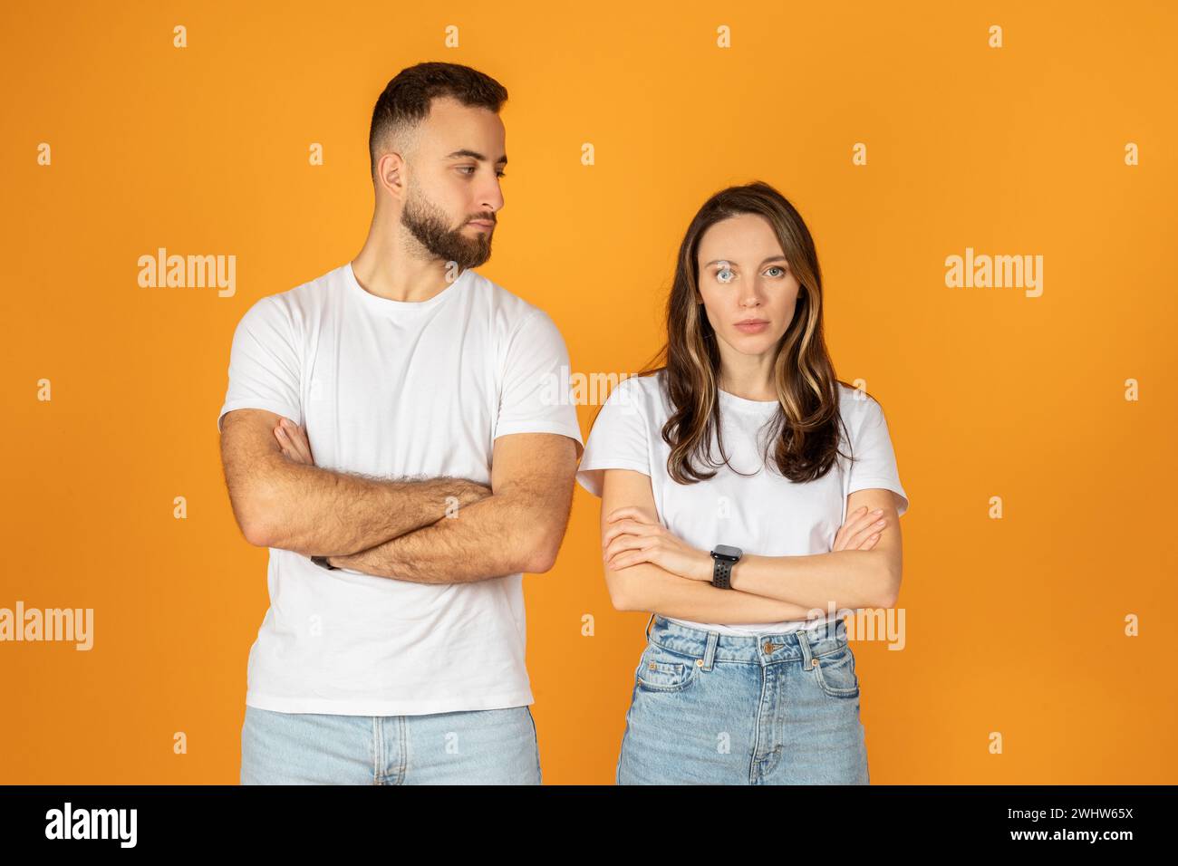 Ein skeptischer junger Mann und eine junge Frau stehen mit überkreuzten Armen und sehen sich an Stockfoto