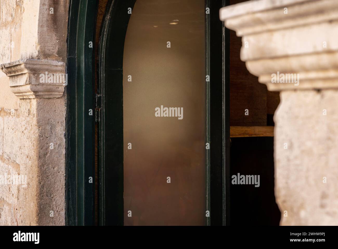 Eingang zum Geschäft oder Restaurant, ein sauberes Fenster dient als Leinwand für Logo-Werbung. Der alte Türrahmen und die Steinmauer sorgen für rustikalen Charme Stockfoto
