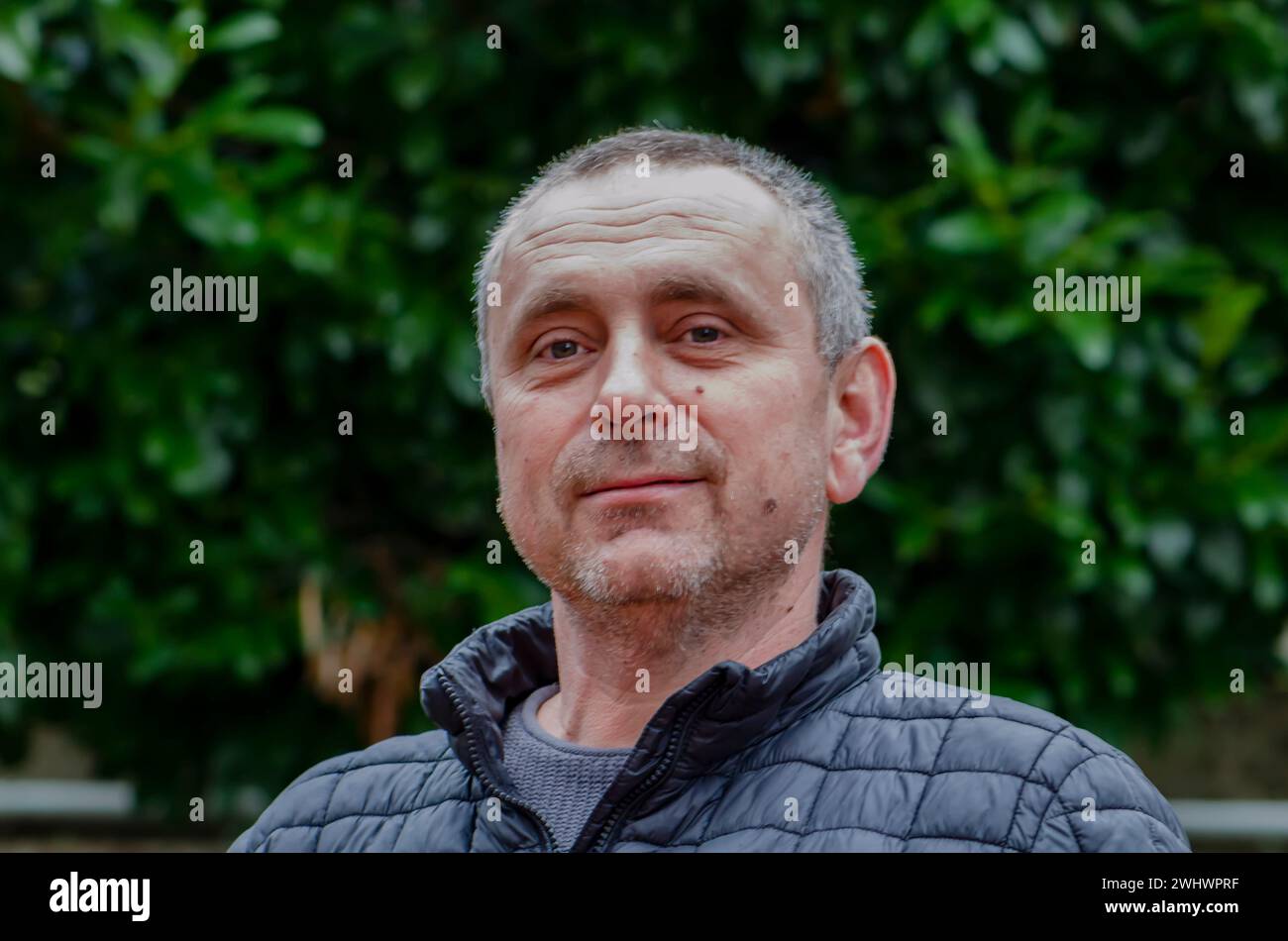 Grauhaariger Mann 45-50 Jahre alt in einer Jacke vor grünem Hintergrund. Stockfoto