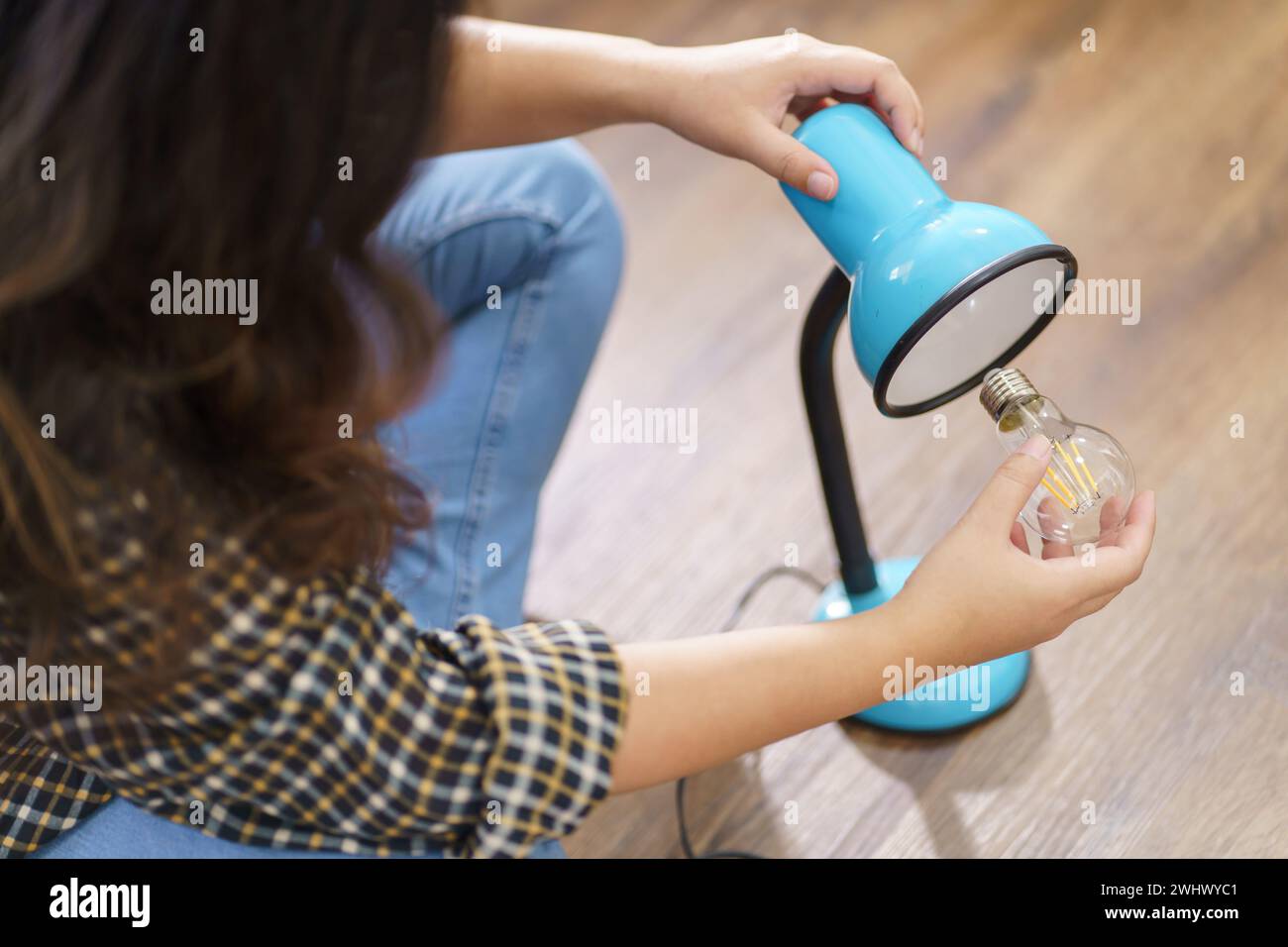 Asiatische Frau wechselt Glühbirne in der Lampenrenovierung mit Ausrüstung zum selbermachen der Glühbirne und Lampe, die auf dem Boden sitzt Stockfoto