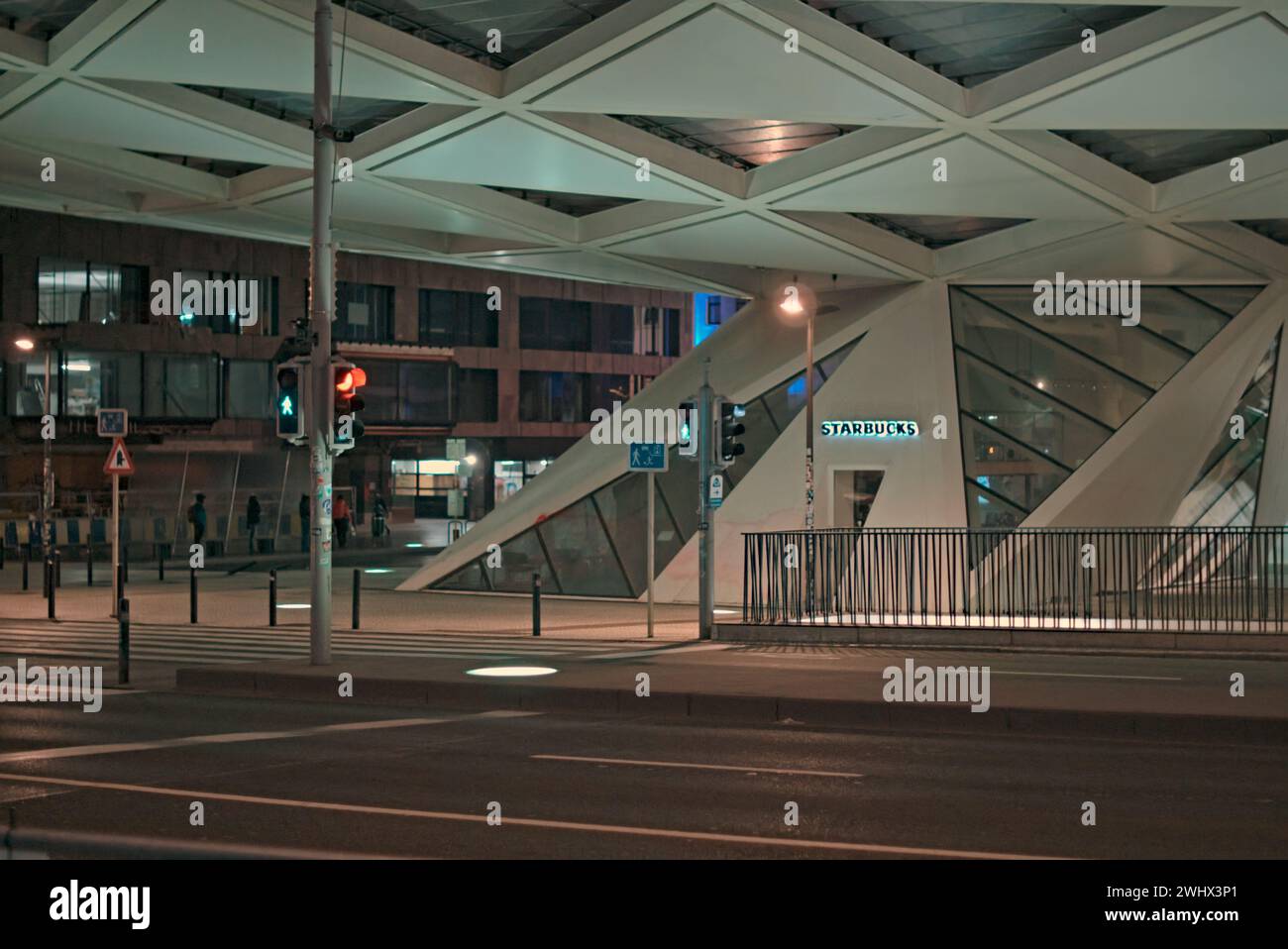 Brüssel, Belgien 5-02-2024. Nachtstraßen von Belgien. Fassade des Starbucks Gebäudes. Beleuchteter Bürgersteig. Silhouetten von Menschen auf der Straße Stockfoto