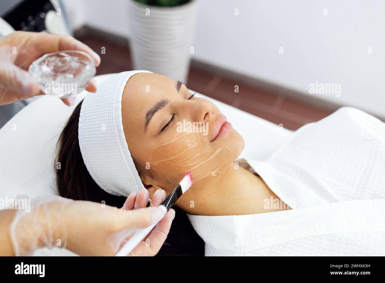 Der Schönheitsmeister wendet eine verjüngende Maske auf das Gesicht des Kunden an. Stockfoto