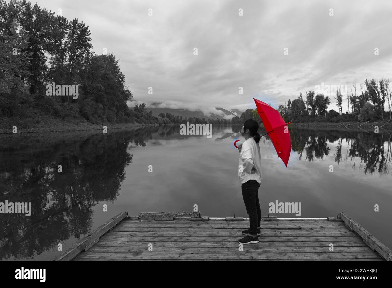 Schwarz-weißes Foto einer Frau auf einem Dock mit einem roten Regenschirm. Stockfoto