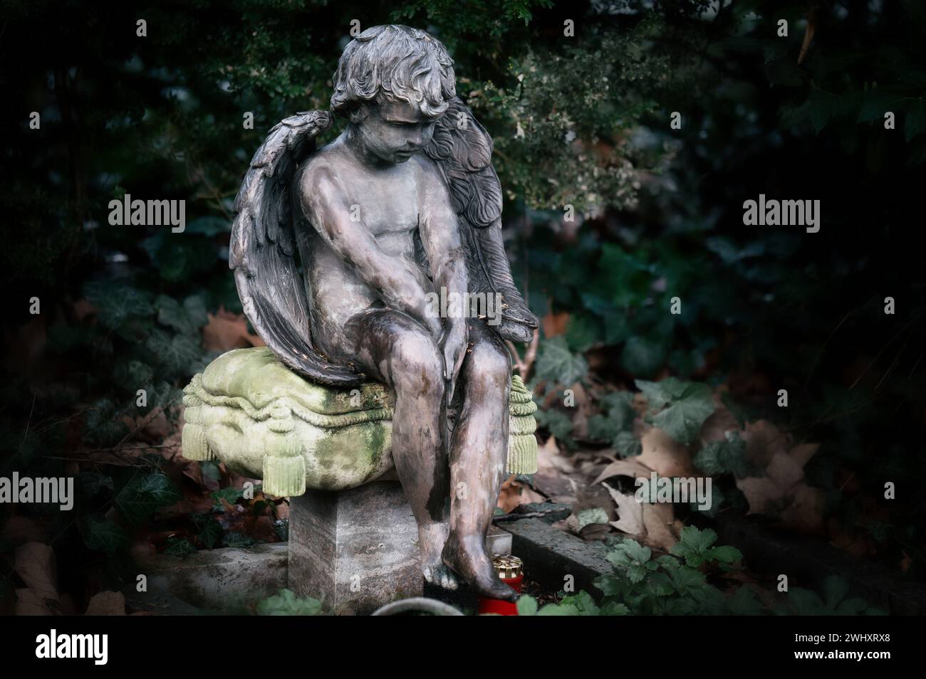 Ein kleiner Engel mit Flügeln sitzt traurig auf einem Steinkissen auf einem Grabstein auf einem Friedhof Stockfoto