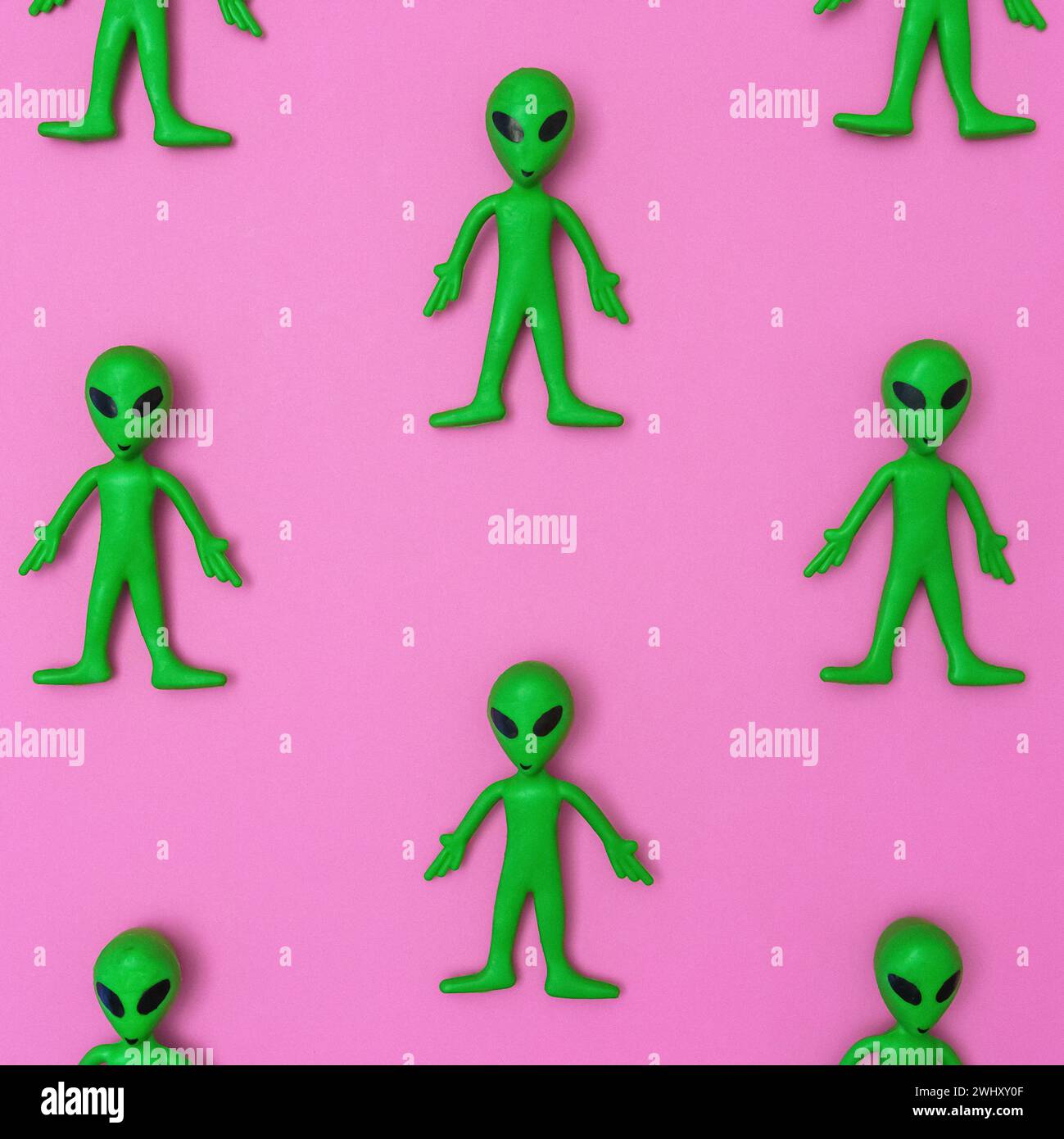 Grüne Alien-Spielzeugpuppen in einem sich wiederholenden Muster auf einem durchgehenden rosafarbenen Hintergrund Stockfoto
