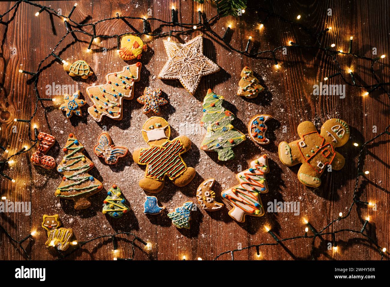Bunte glasierte Kekse auf einem bemehlten Tisch zwischen glühenden Girlanden. Draufsicht Stockfoto