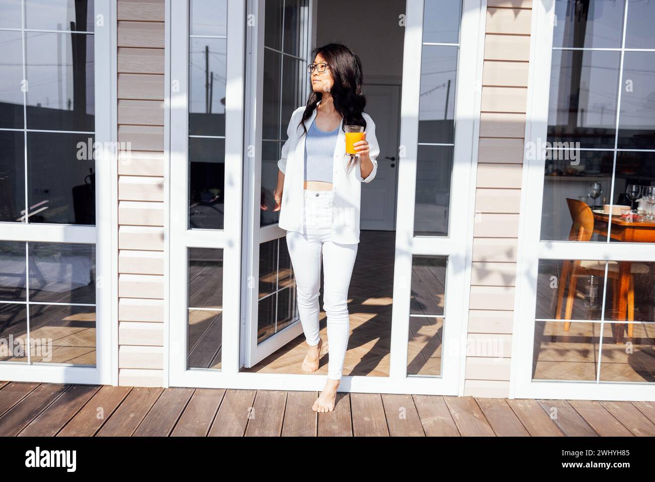 Die junge süße asiatische Frau öffnet die Glastür und geht auf die Veranda. Stockfoto