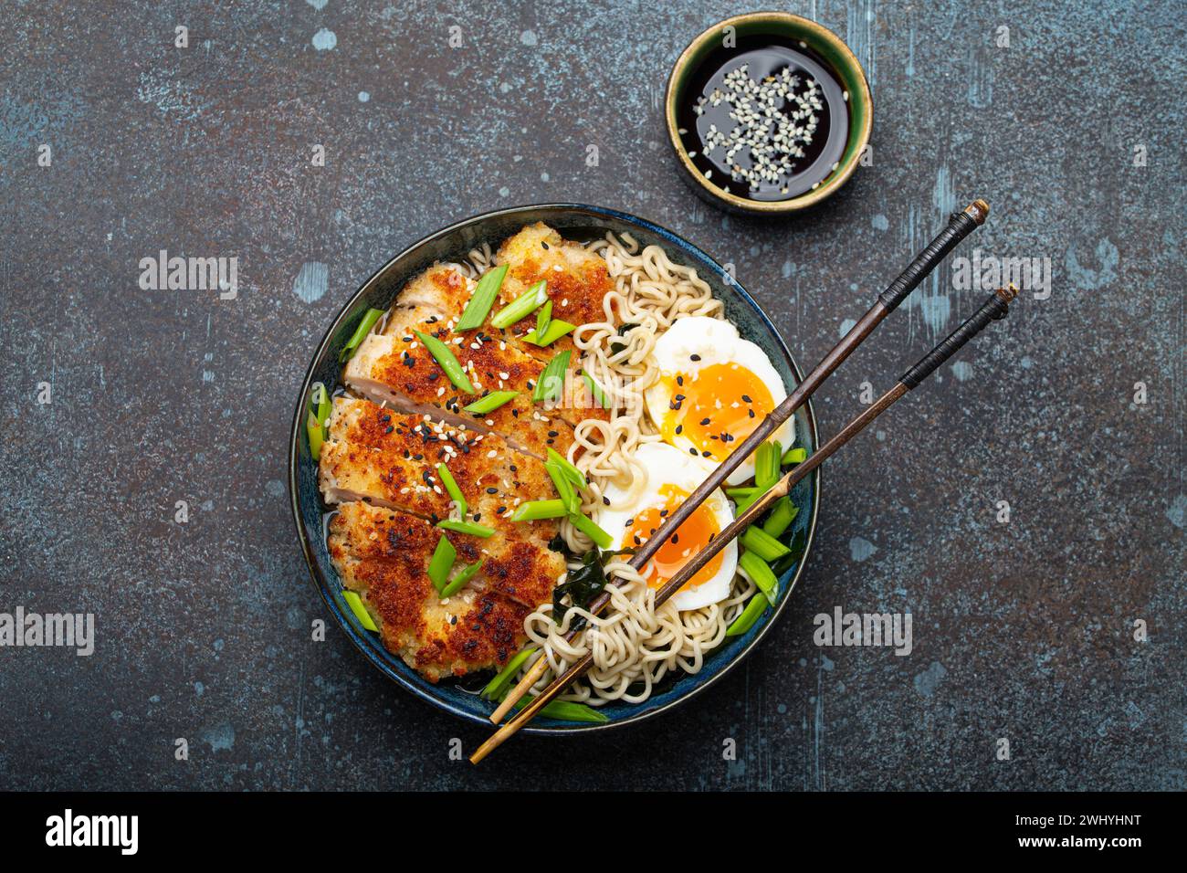 Asiatische Nudeln Ramen-Suppe mit frittiertem Panko-Hähnchenfilet und gekochten Eiern in einer Keramikschale mit Häckslerstäbchen, Sojasauce auf Sto Stockfoto