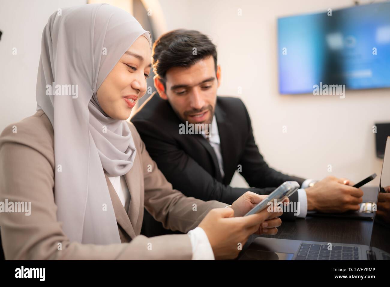 In einem modernen Büro sprechen eine Hijab-Geschäftsfrau und ein Geschäftsmann während eines Meetings und benutzen ein Smartphone. Stockfoto