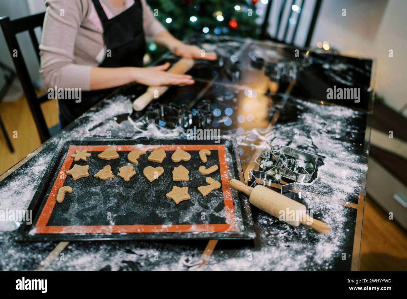 Koch rollt den Teig auf dem Tisch neben dem Tablett mit ausgeschnittenen Keksen aus. Abgeschnitten Stockfoto