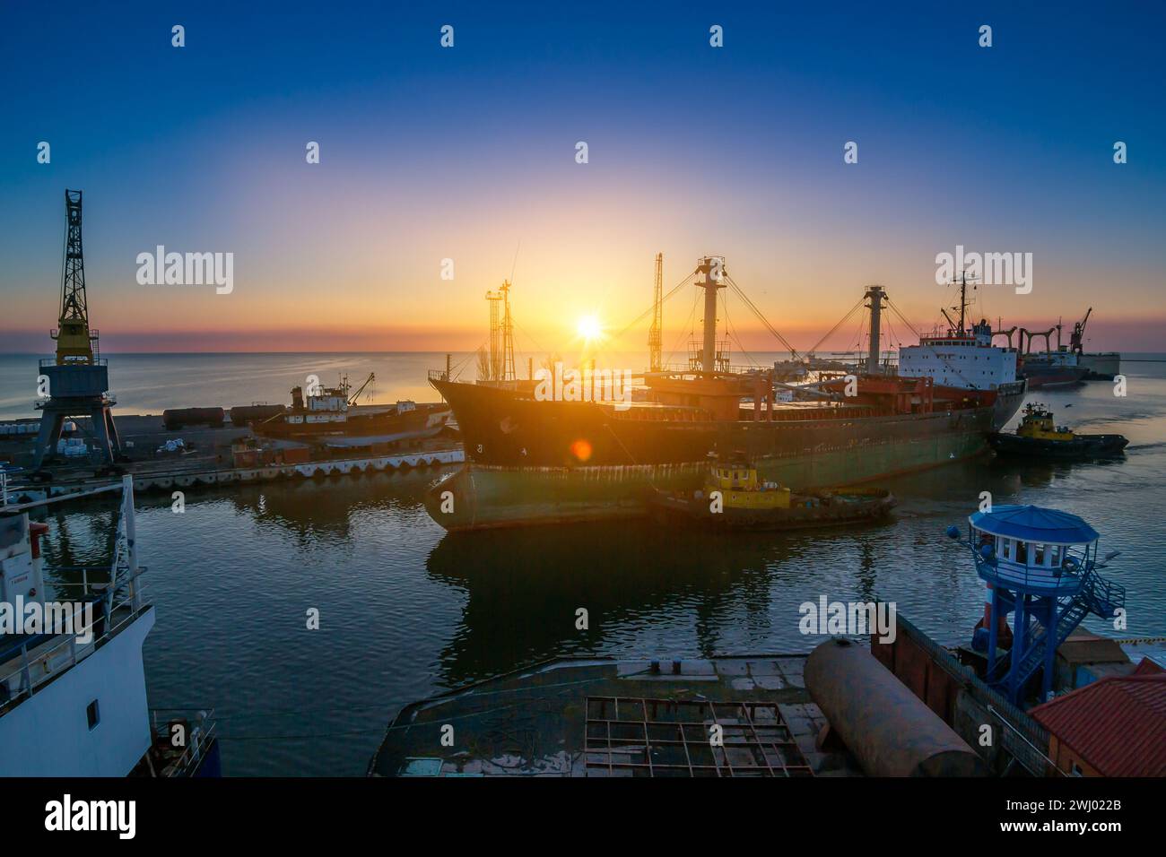 Sonnenaufgang, geschäftiger Seehafen, Frachtschiffe an Liegeplatz, Kräne zum Entladen bereit. Logistikzentrum für den Welthandel, Frachter Ready International Stockfoto