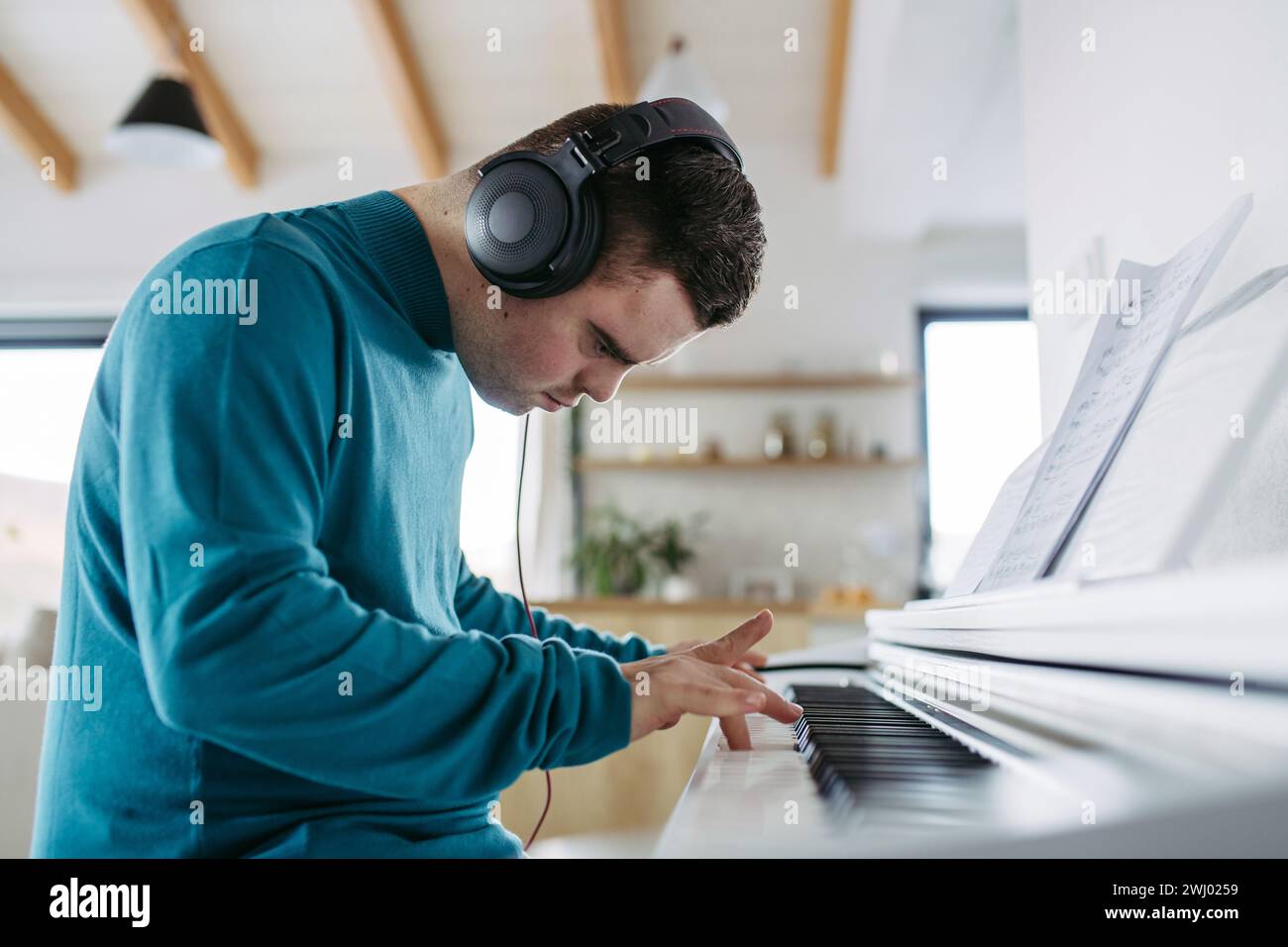 Junger Mann mit Down-Syndrom, der am Klavier spielt und seine Musik über Kopfhörer hört. Stockfoto