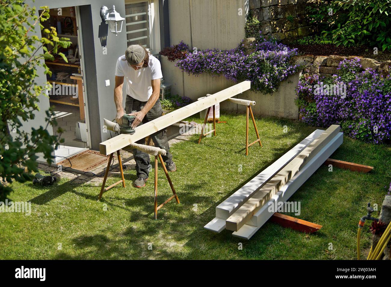 Vorbereitung Schleifen von Holzarbeiten im Freien. Arbeiten mit einem Exzenterschleifer im Frühjahr. Zimmerei Stockfoto
