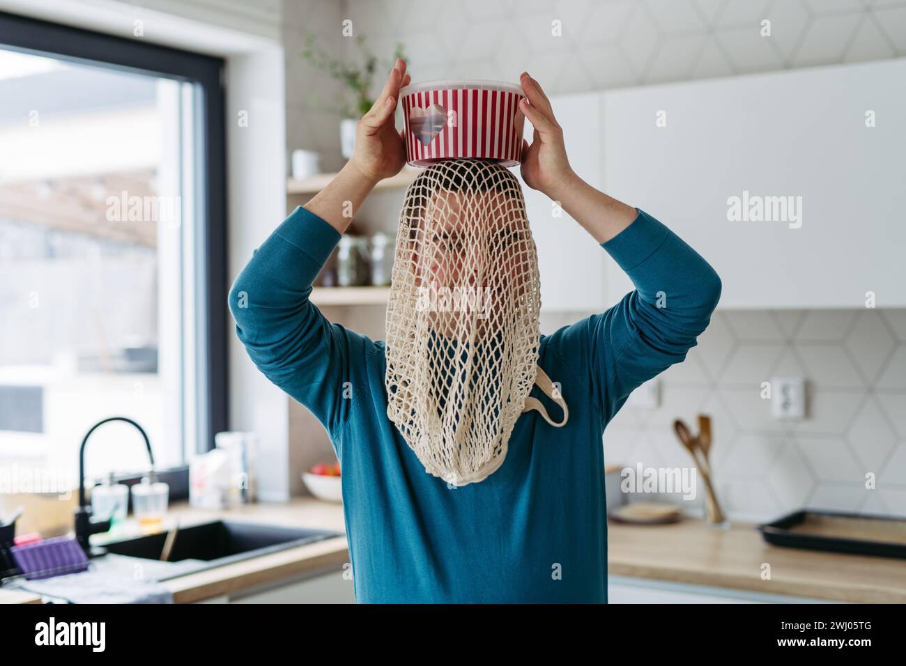 Porträt eines jungen Mannes mit Down-Syndrom, der lustig ist, einen Netzbeutel auf dem Kopf hat und Popcorn-Eimer hält. Stockfoto