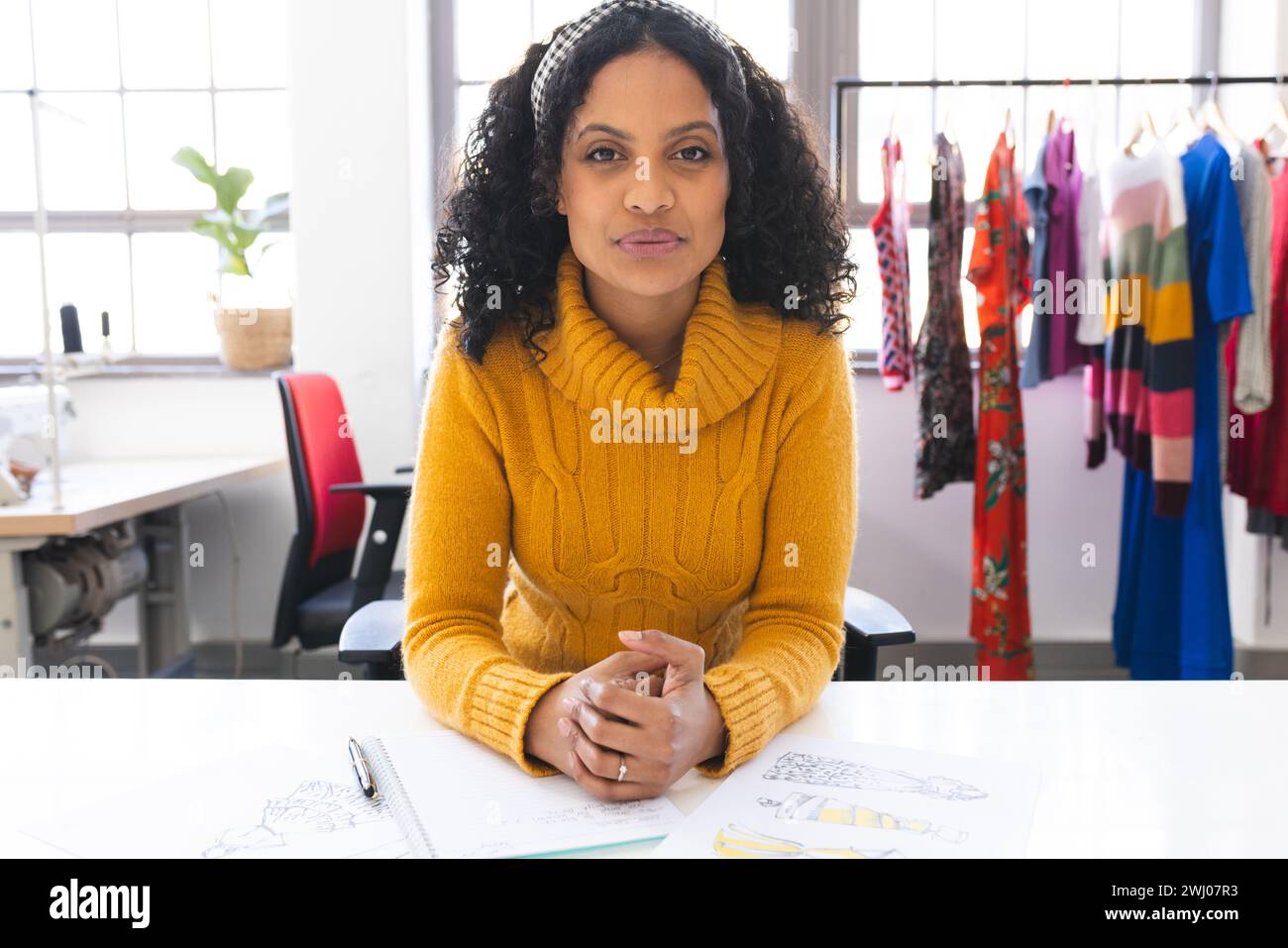 Fokussierte birassische Modedesignerin, die Videoanrufe am Schreibtisch im Studio hat. Mode, Design, Kreativität, Kleidung und Kleinunternehmen, Kommunikation, Stockfoto
