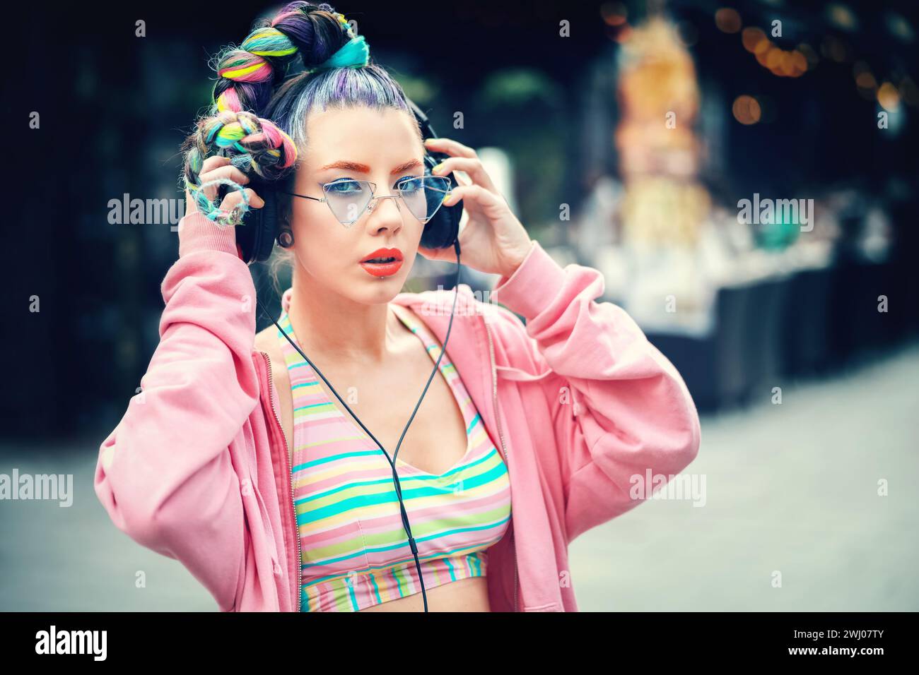 Porträt eines urbanen Gen z Mädchens mit trendiger Frisur Genießen Sie Musik auf großen Kopfhörern während des Street Music Festivals Stockfoto