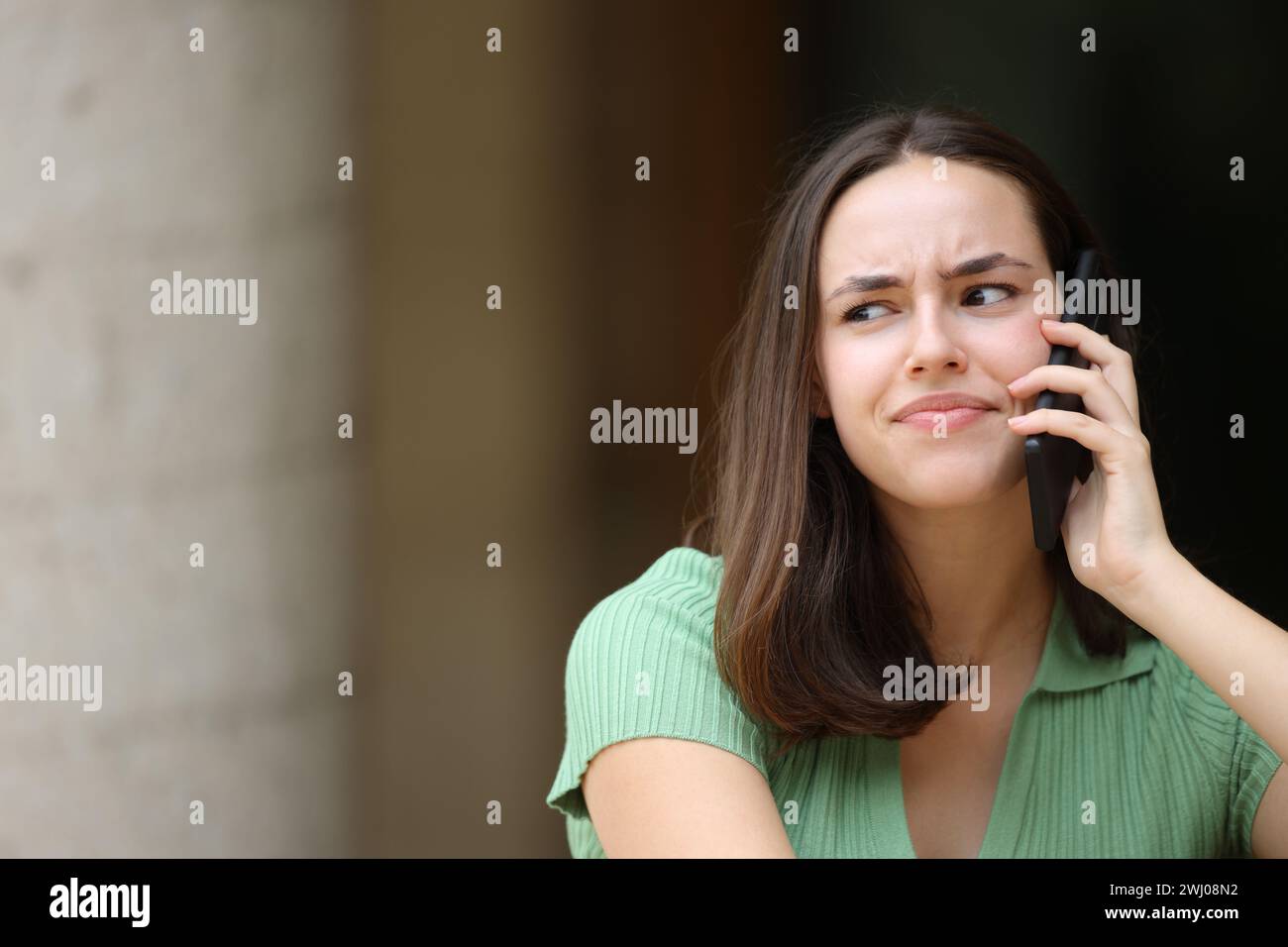 Vorderansicht Porträt einer misstrauischen Frau, die auf der Straße telefoniert Stockfoto
