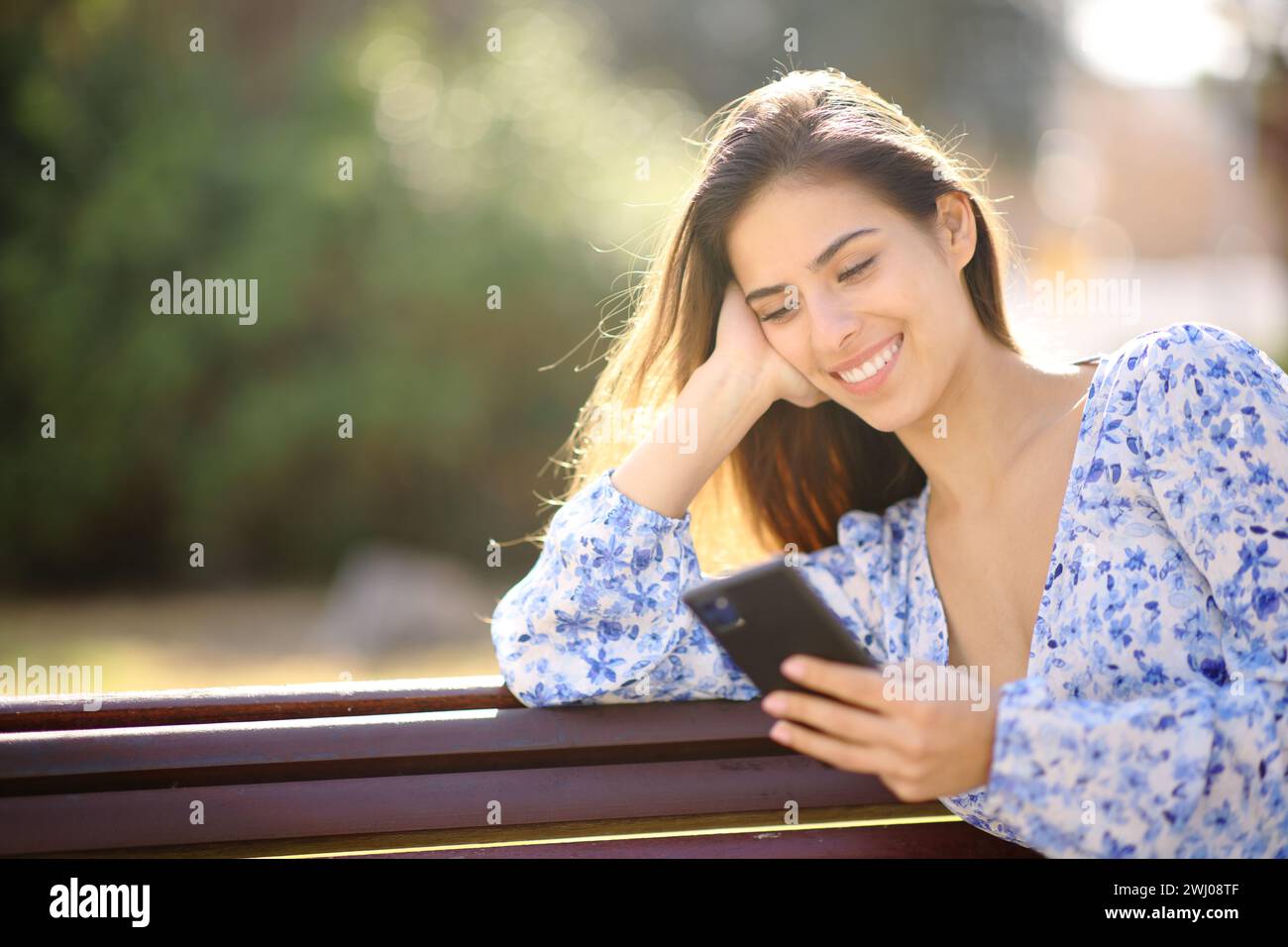 Glückliche Frau, die im Garten sitzt und Telefoninhalte überprüft Stockfoto