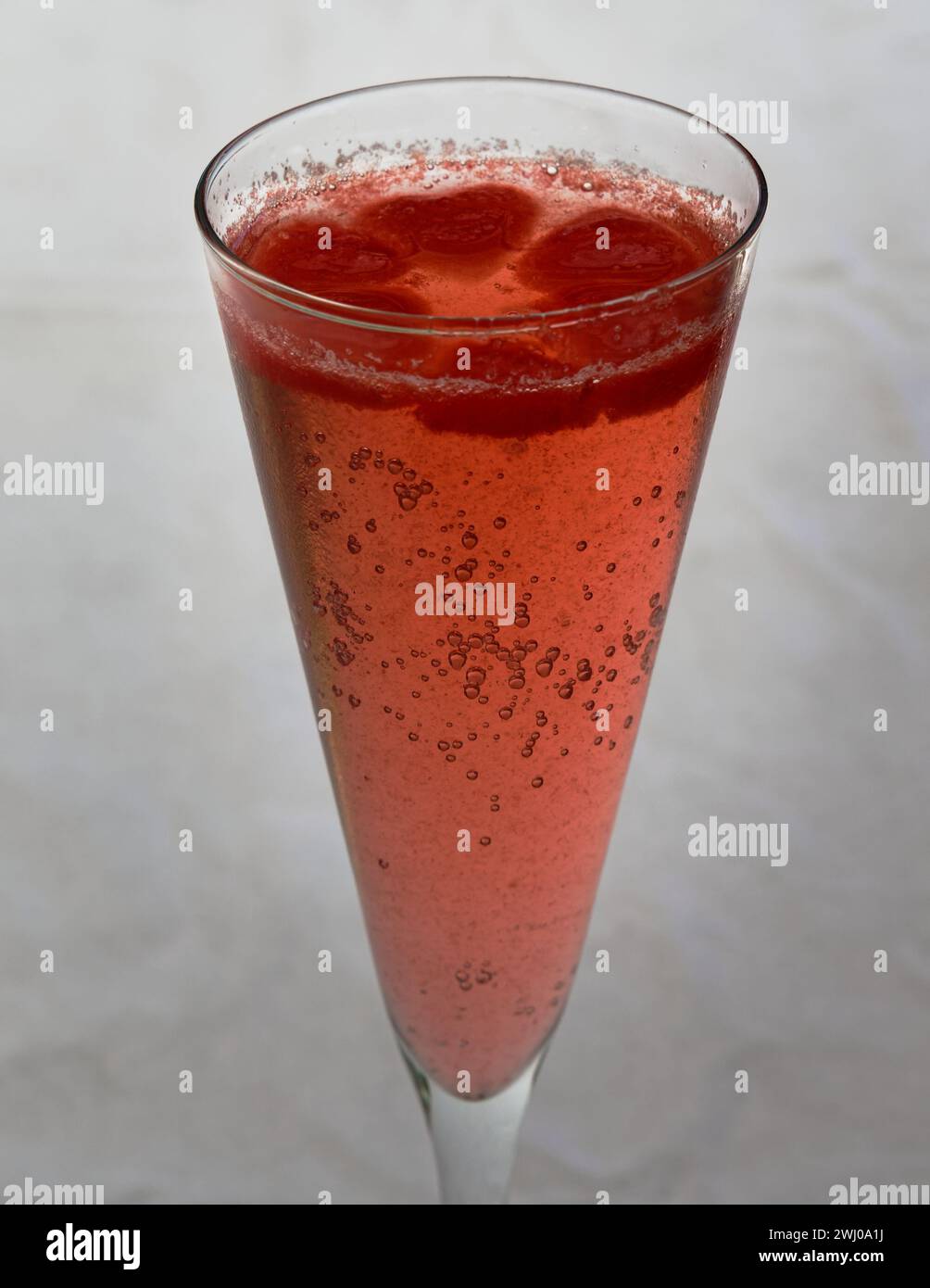 Rosafarbene Eiswürfel schweben auf einem Glas Blasen in einer Sektflöte, Stockfoto