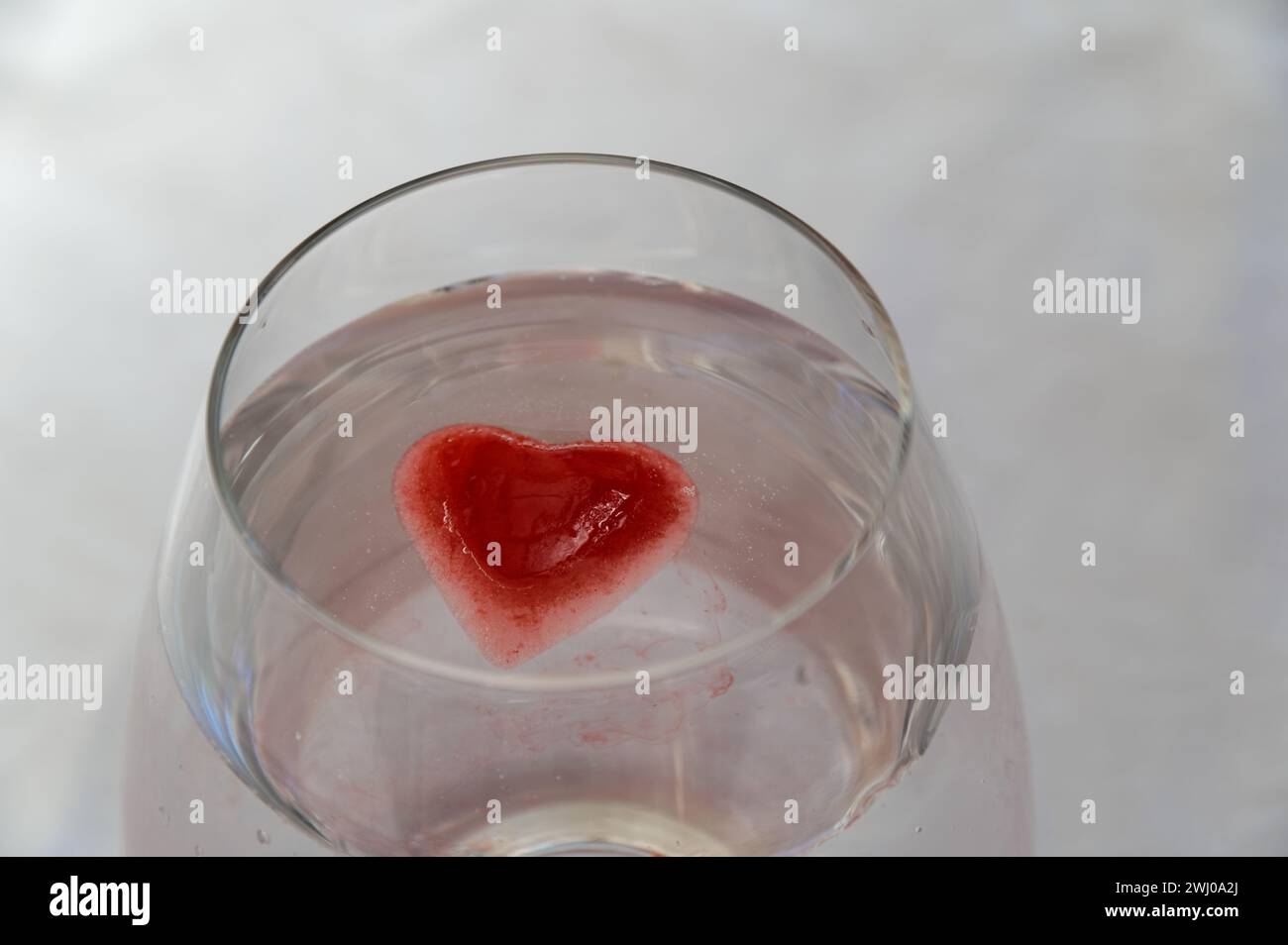 Ein rosafarbener Eiswürfel schmilzt mit der klaren Flüssigkeit im Glas Stockfoto
