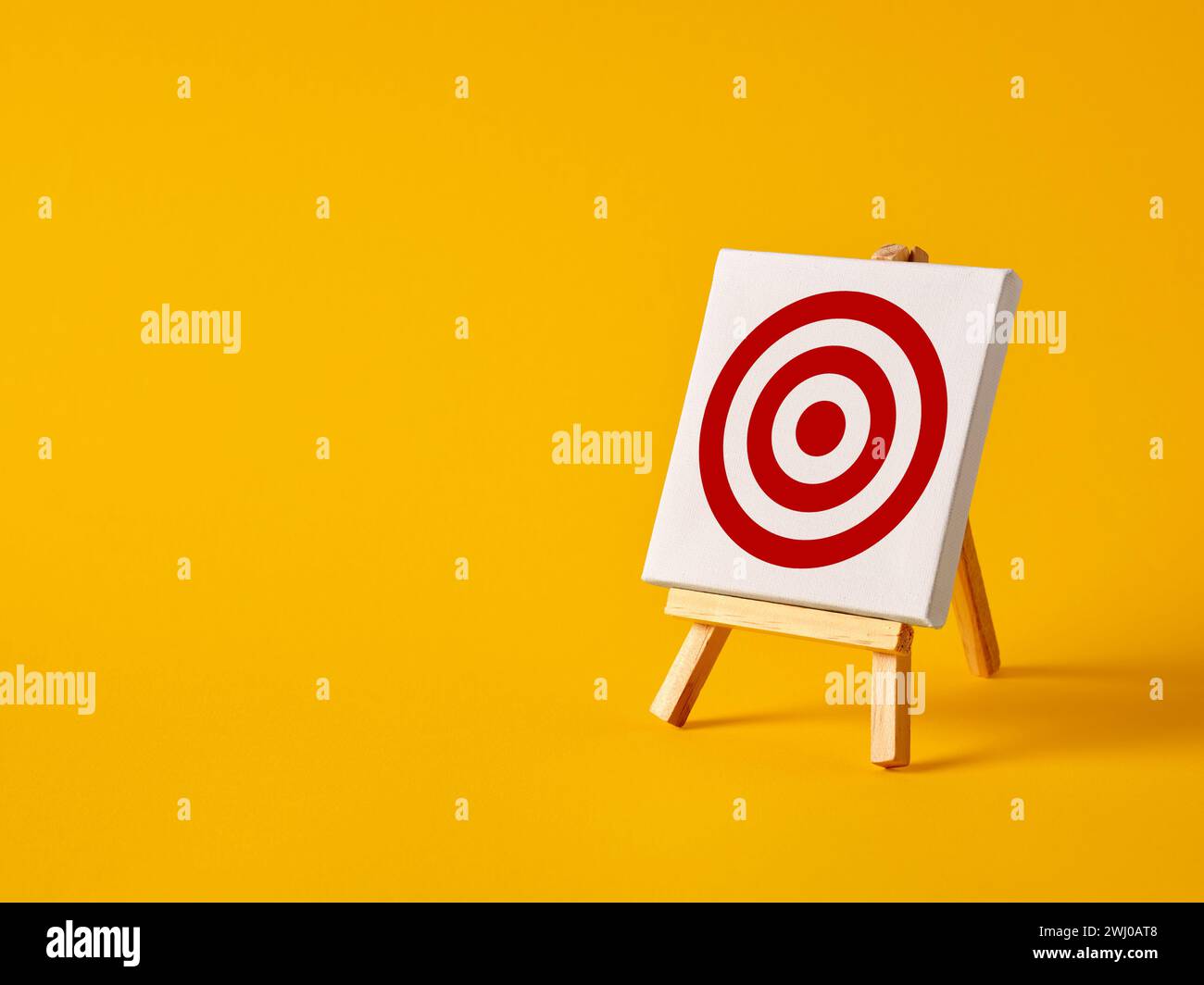 Eine Leinwand mit Zielsymbol auf einer Staffelei mit gelbem Hintergrund und Kopierraum. Erreichung der Geschäftsziele. Das Unternehmen festlegen und anvisieren Stockfoto