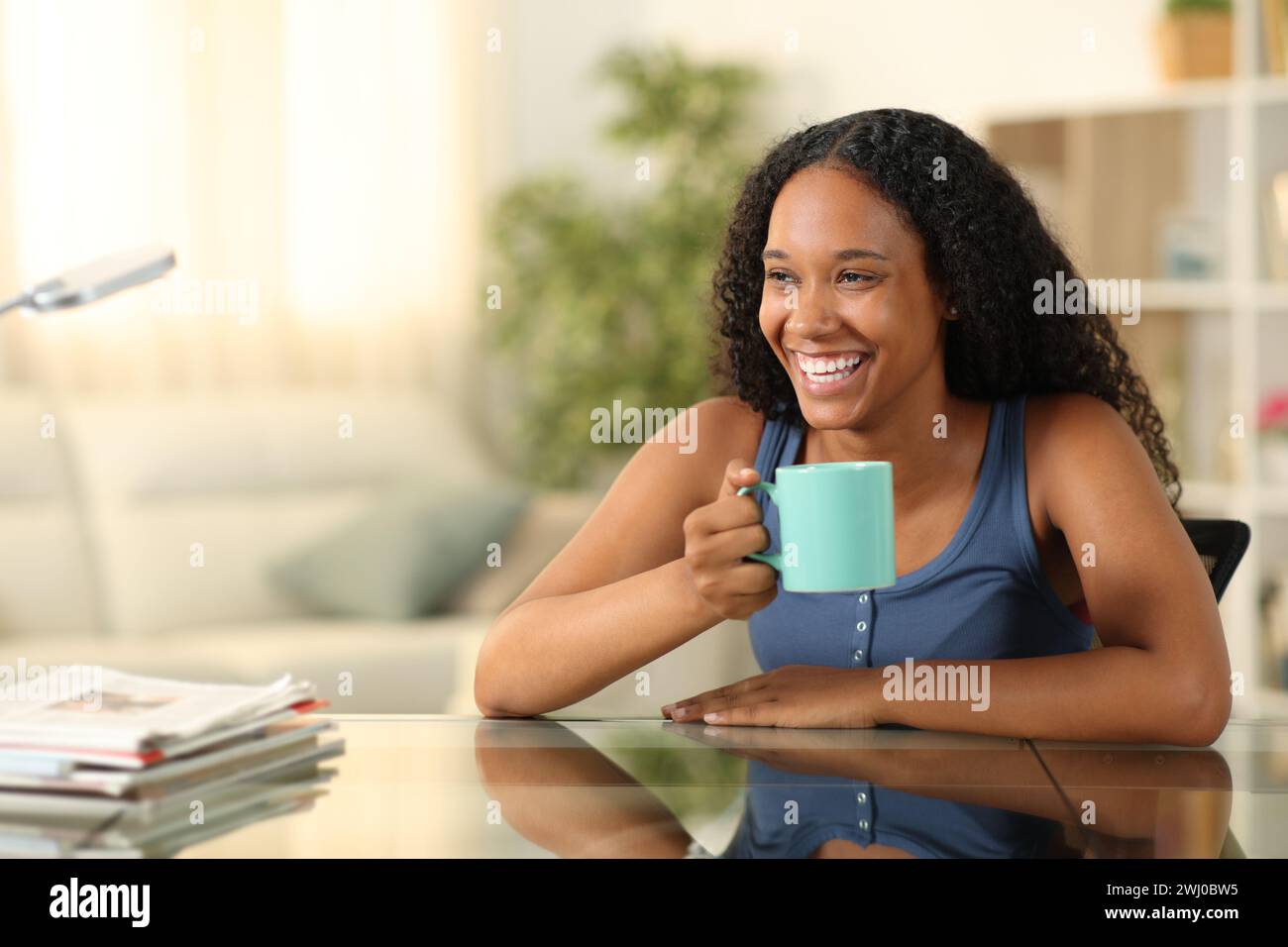 Glückliche schwarze Frau trinkt Kaffee und lacht zu Hause Stockfoto