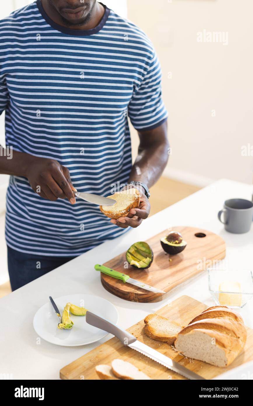 Mittelteil des afroamerikanischen Mannes, der Toast mit Avocado in der Küche, Kopierraum Stockfoto