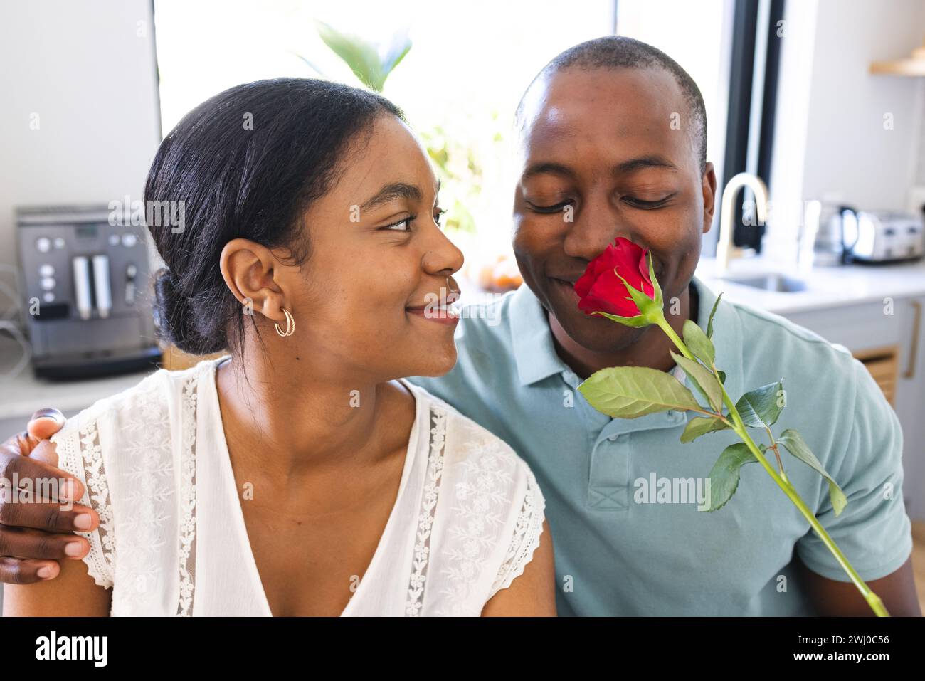 Ein junger afroamerikanischer Mann überrascht die birassische Frau mit einer Rose zu Hause Stockfoto